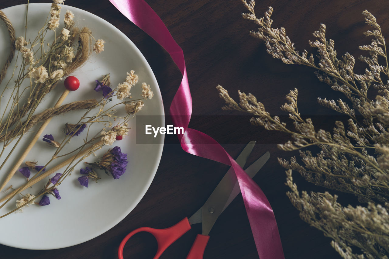 Directly above shot of ribbon and scissors amidst dried plants on table