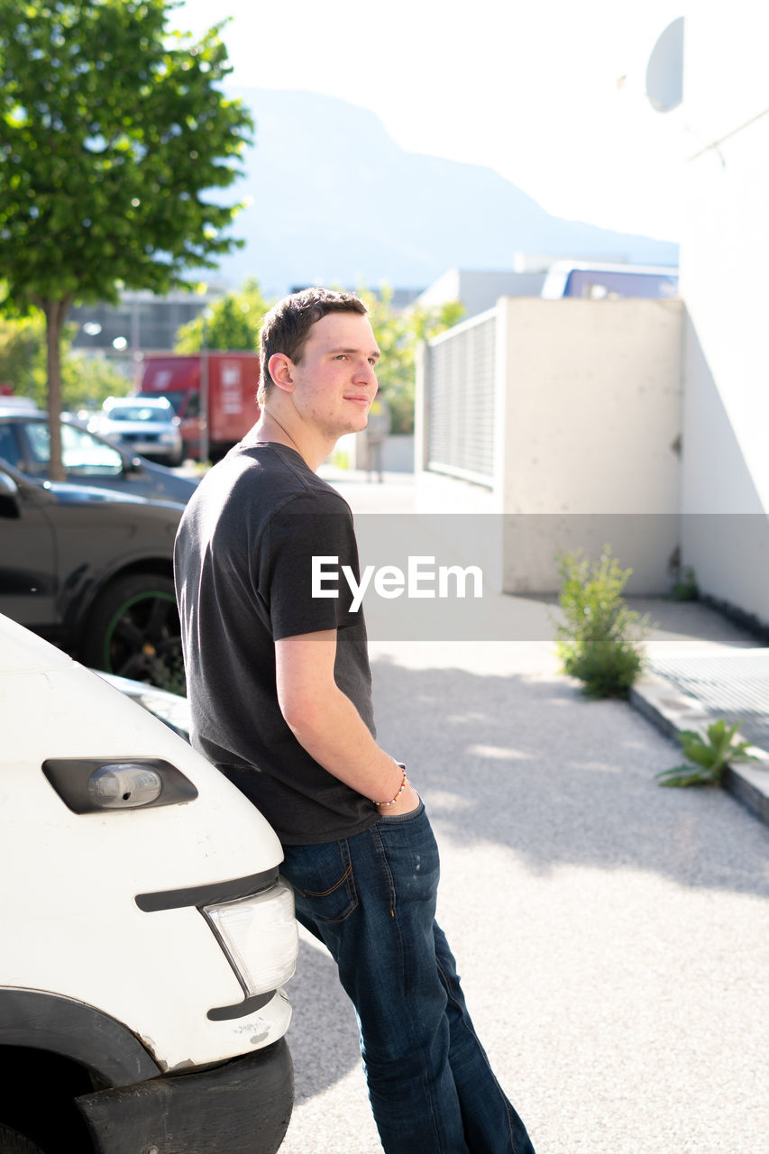 Side view of young man leaning on car