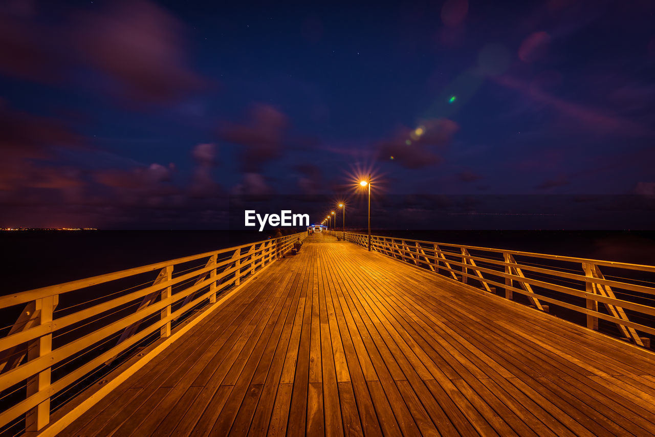 Illuminated bridge over sea against sky at night