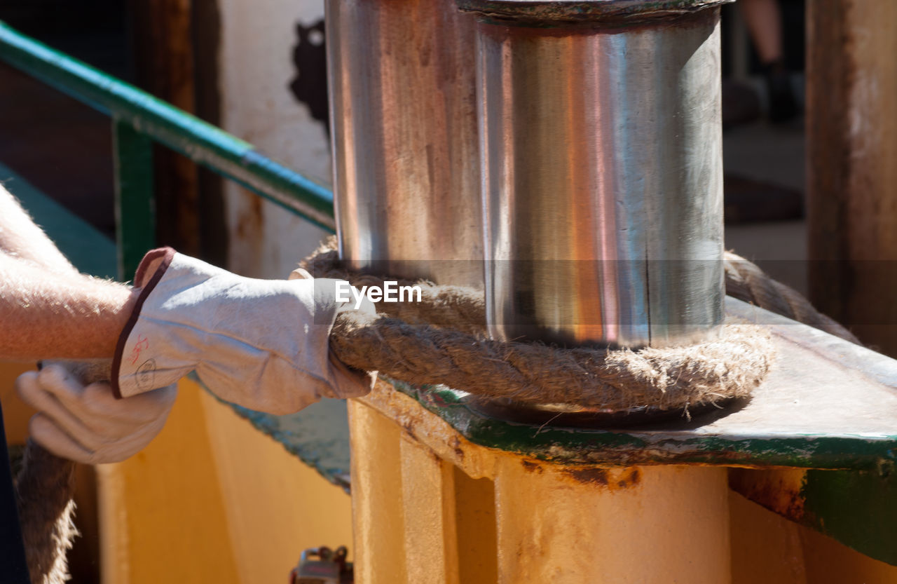 Cropped image of worker tying rope on metal