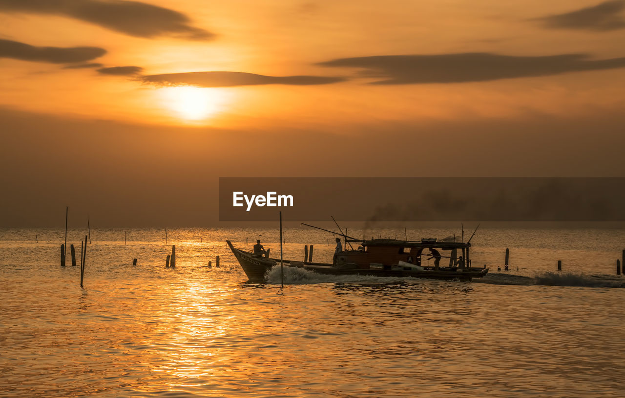 Fishermen in boat over sea against sunset sky