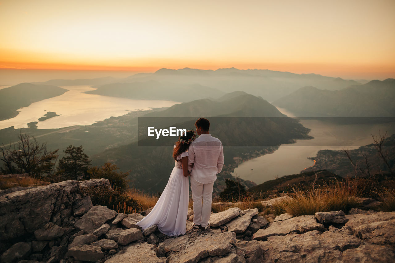 Rear view of couple standing on rock at beach against sky