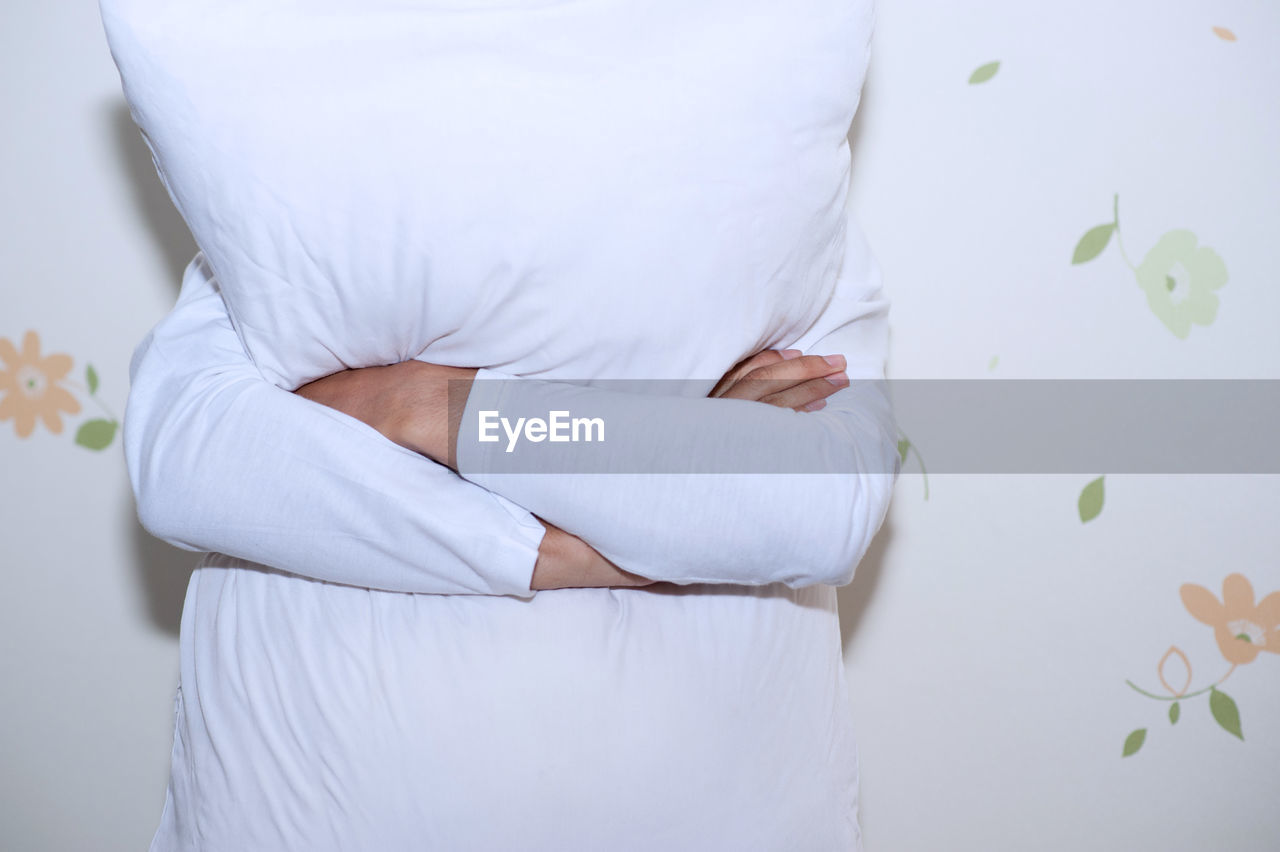 Midsection of woman holding pillow while standing against wall