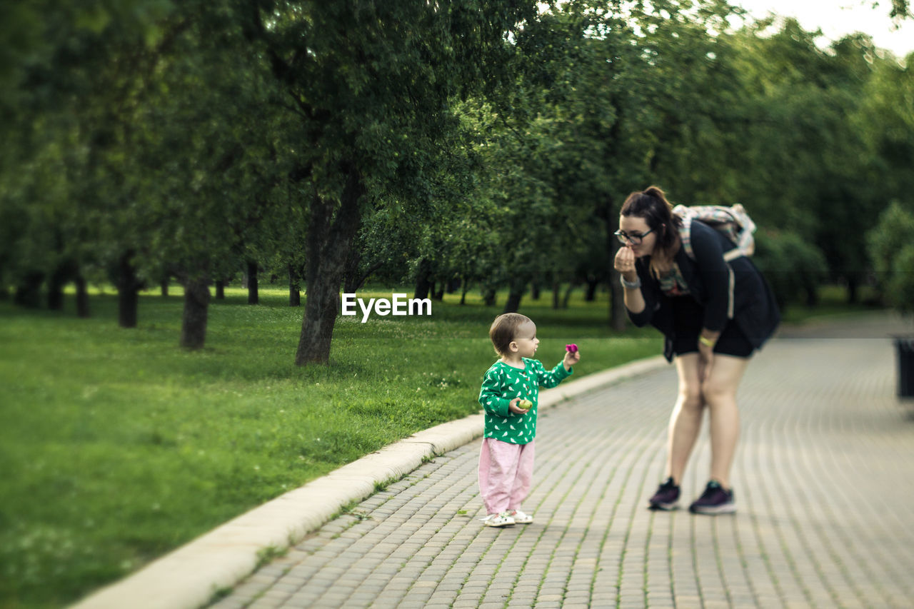 Mother talking with daughter while standing on footpath at park