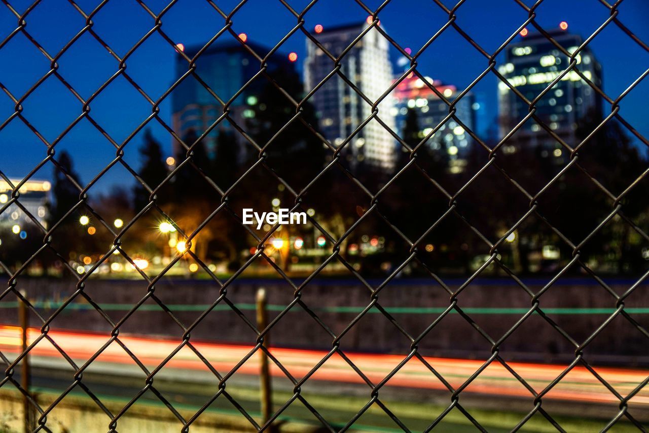 Full frame shot of chainlink fence against illuminated city at night