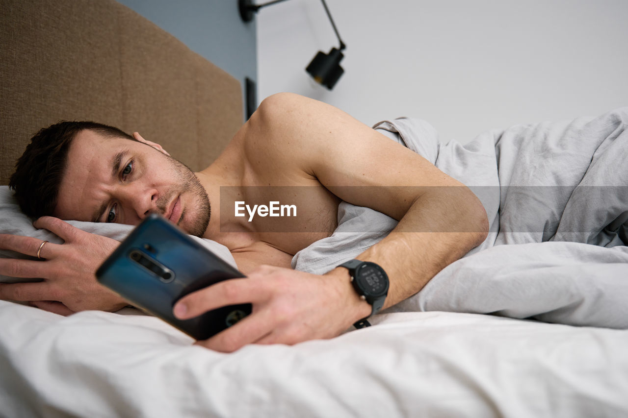 Phone addiction. man lying in bed with smartphone