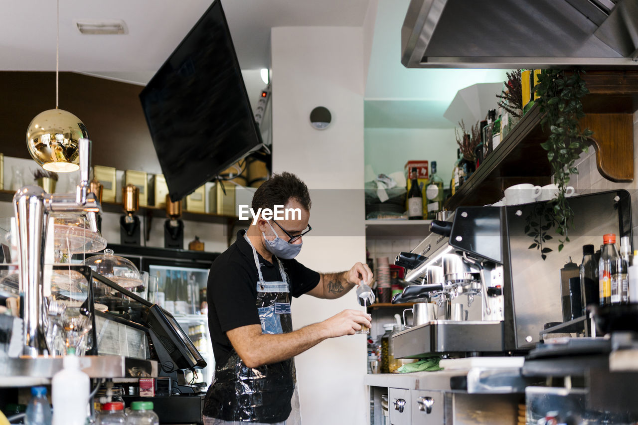 Male barista wearing protective face mask while working in cafe during covid-19 crisis