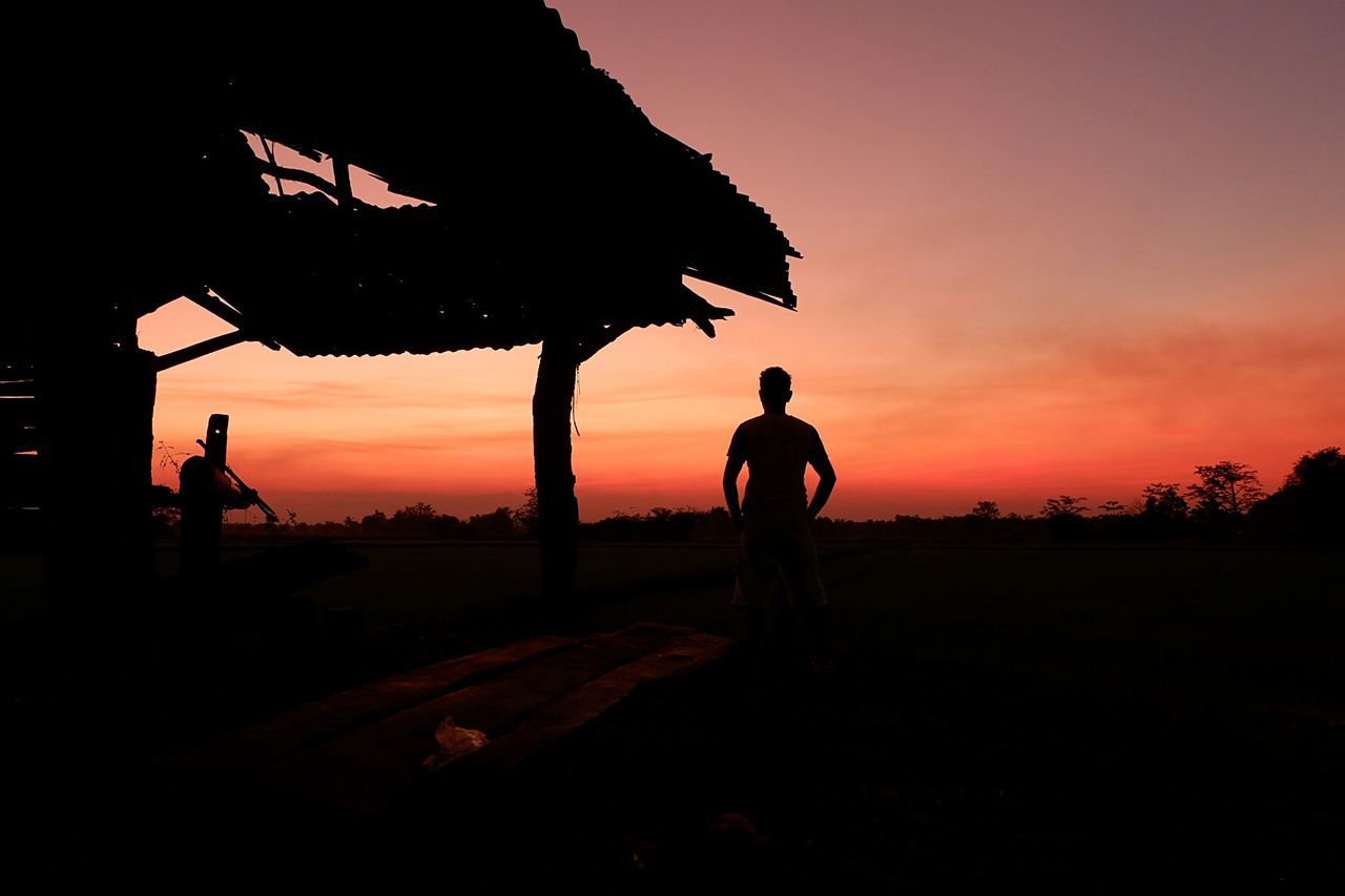 Silhouette mature man standing on field against sky during sunset
