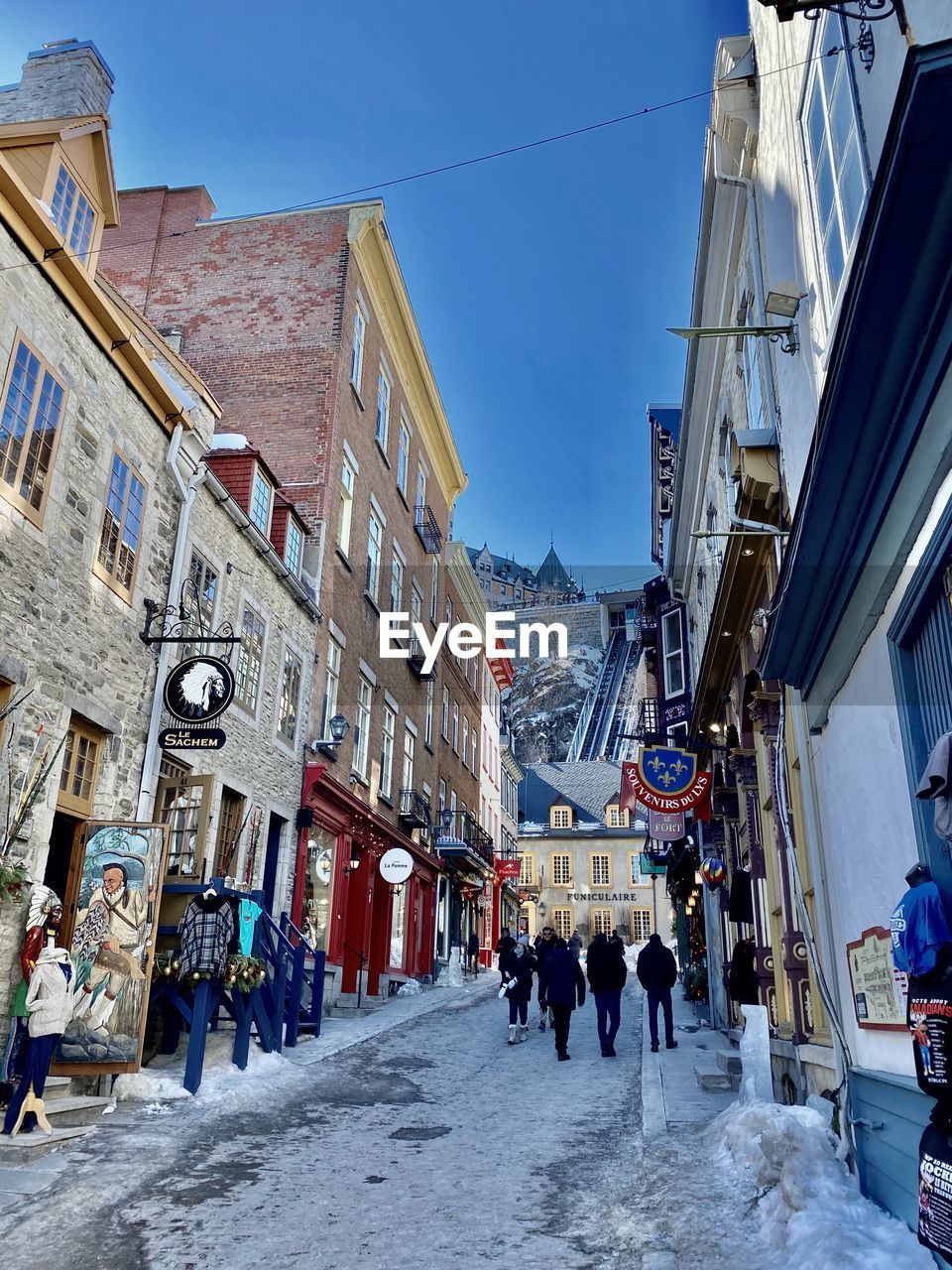 PEOPLE WALKING ON STREET AMIDST BUILDINGS AGAINST SKY