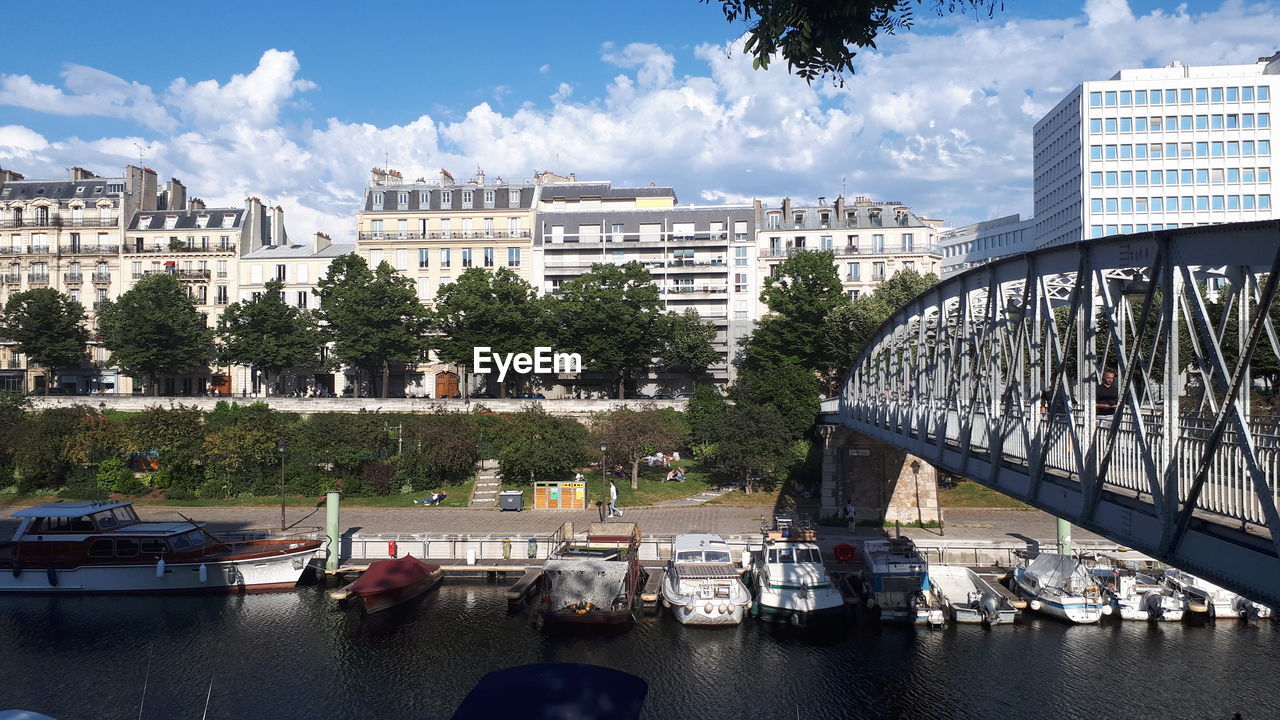 Bridge over river by buildings in city against sky