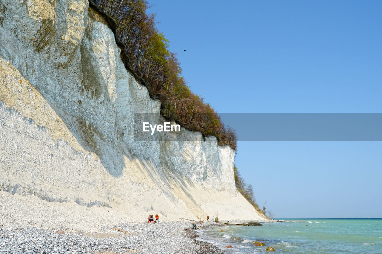 Low angle view of chalk cliff by sea against clear blue sky