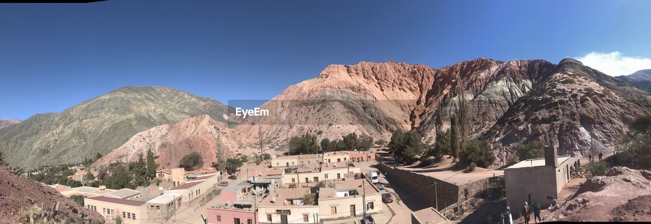 PANORAMIC VIEW OF BUILDINGS AND MOUNTAINS AGAINST CLEAR BLUE SKY