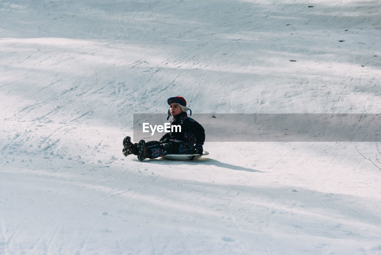 Cute boy sledding on snow covered field during winter