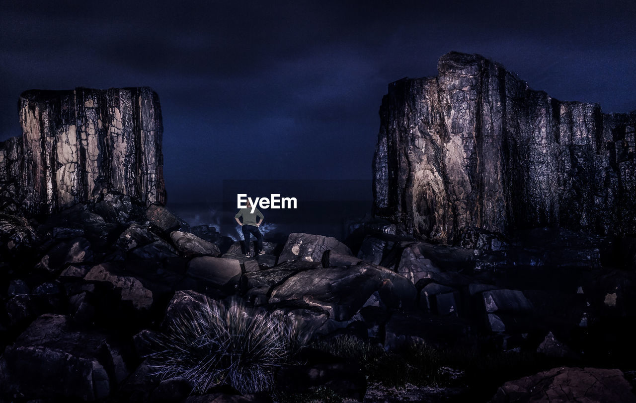 Rear view of woman sitting on rock at beach against sky at night