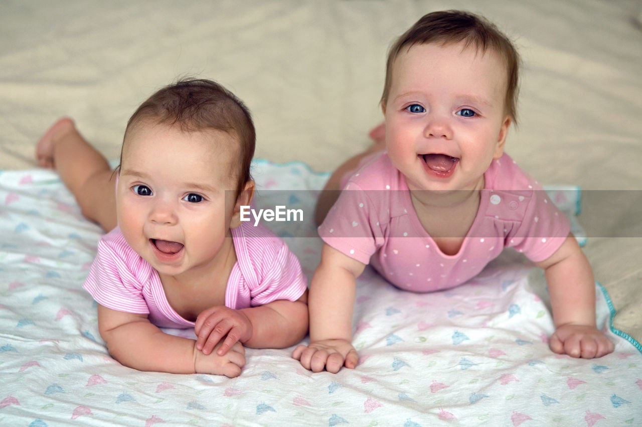 Two sisters twins baby in pink clothes lying on the bed in a diaper