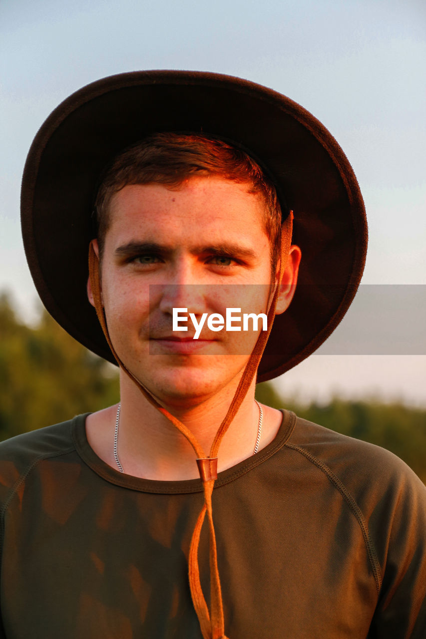 Young man smiling farmer in cowboy hat at agricultural field on sunset with sun flare. portrait 