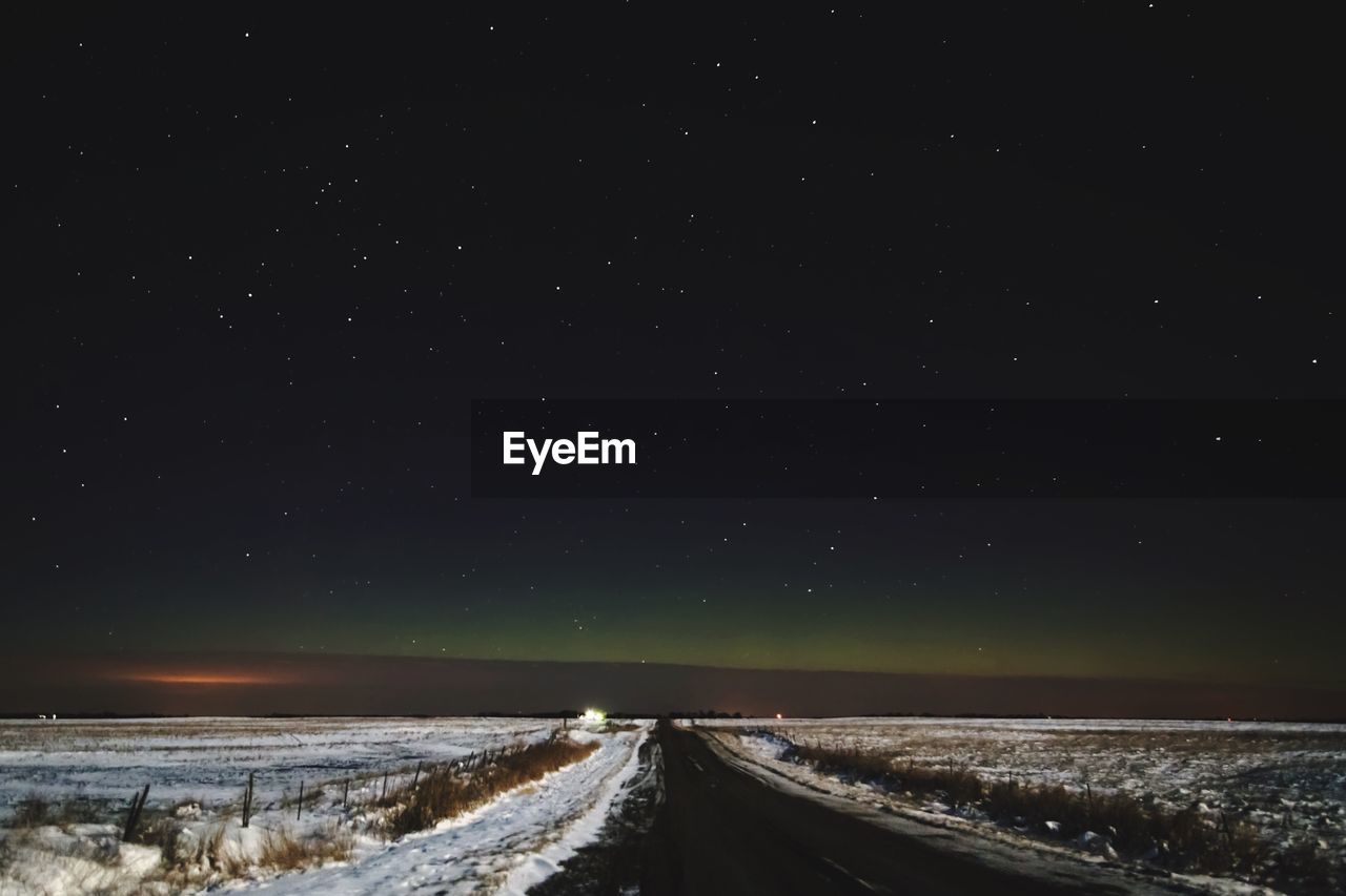 Empty road amidst landscape against star field during winter