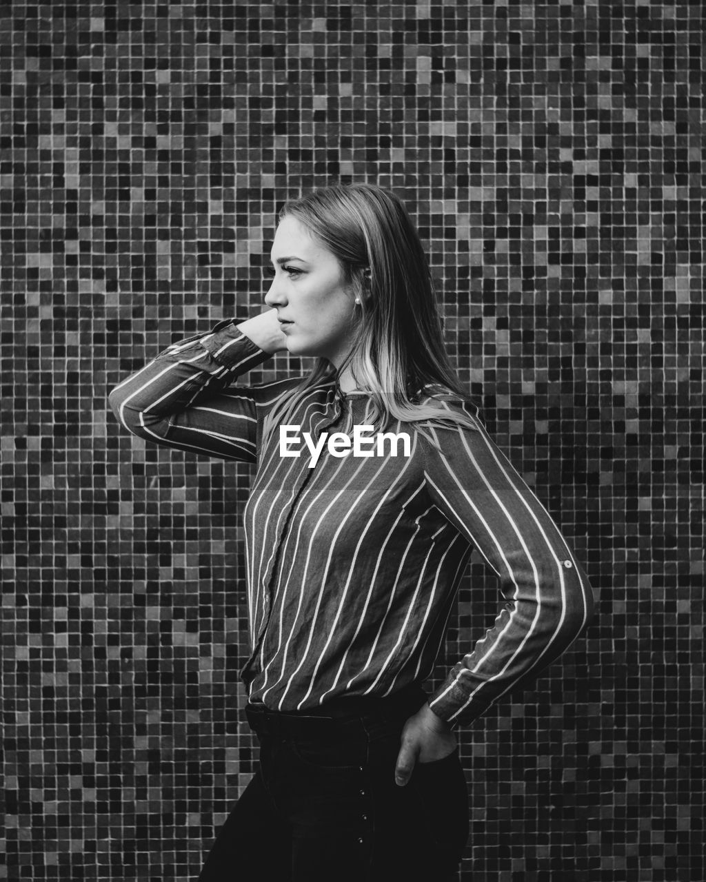 Young woman looking away while standing against wall