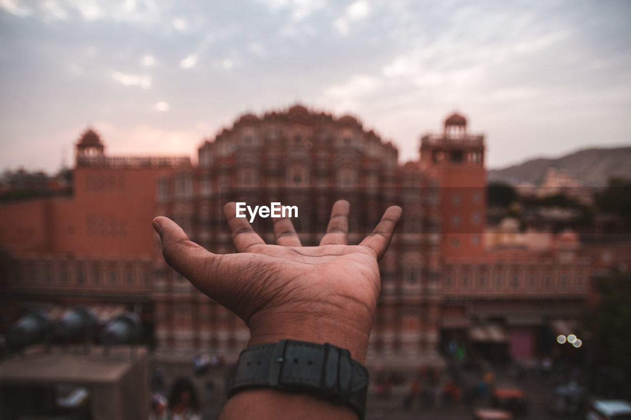 Cropped image of person hand against building in city against sky
