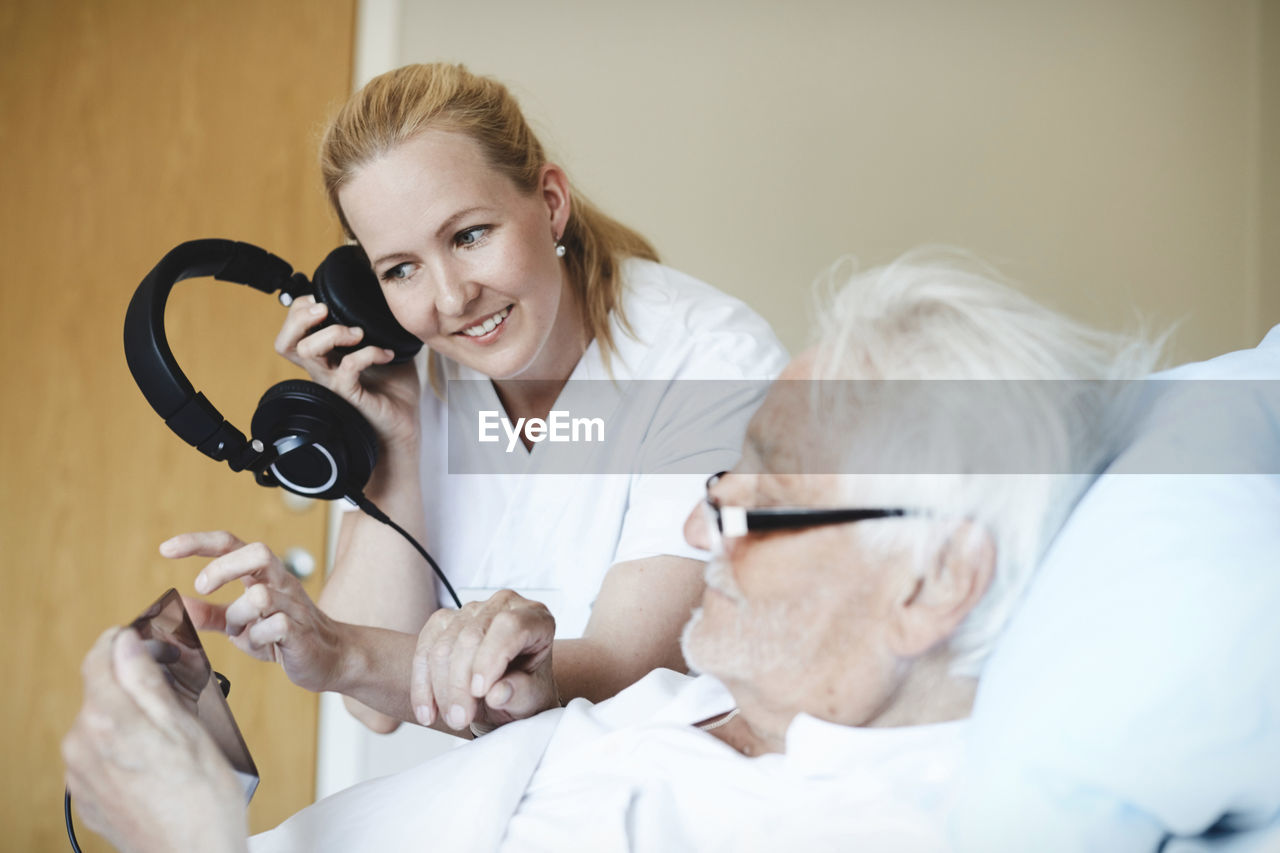 Smiling female nurse listening music through headphones while using digital tablet in hospital ward