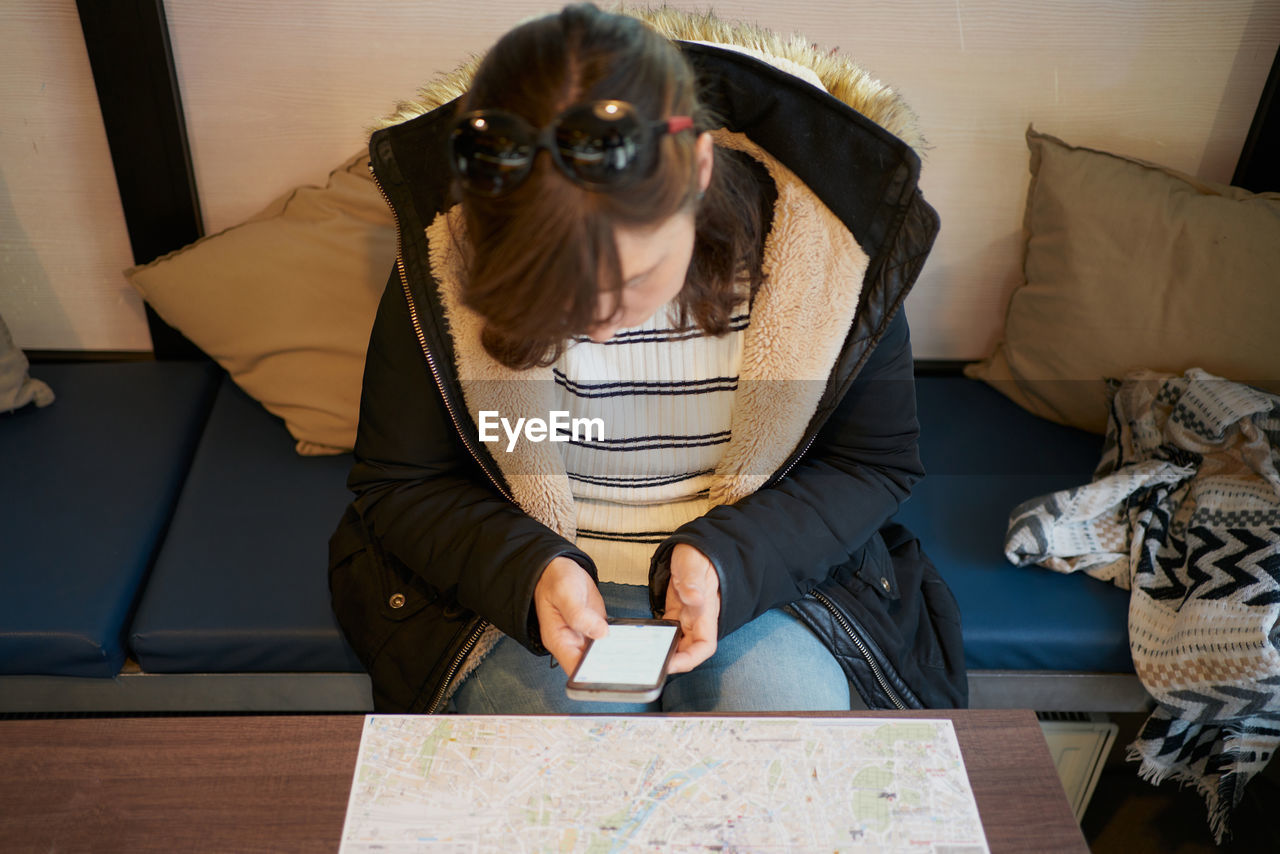 Woman sits looking at her phone in front of a tourist map person