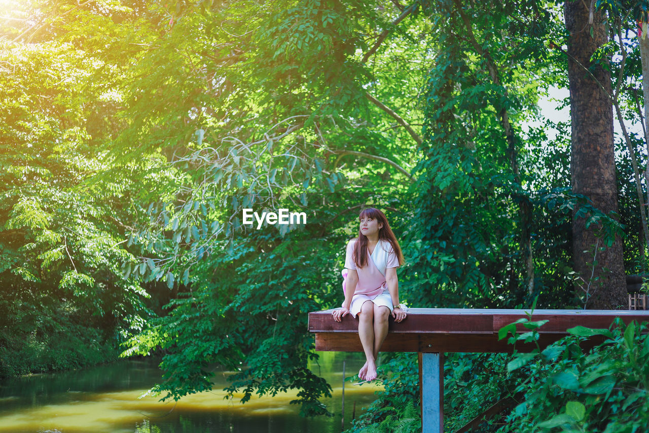 WOMAN SITTING IN FOREST AGAINST TREES