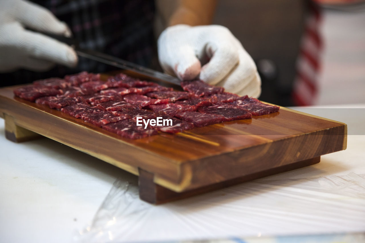 Midsection of man cutting meat on chopping board in kitchen