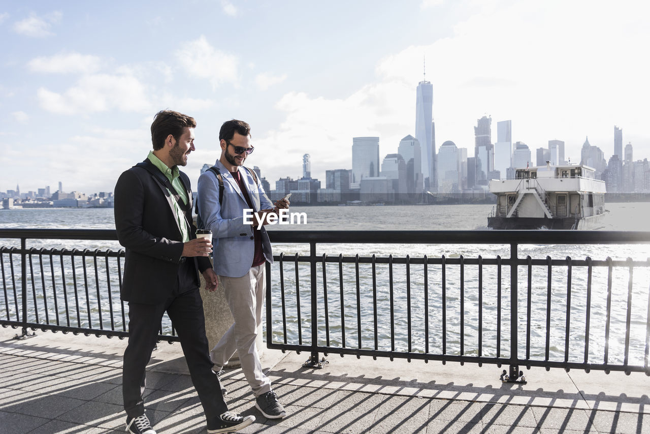 Usa, two businessmen walking at new jersey waterfront with view to manhattan
