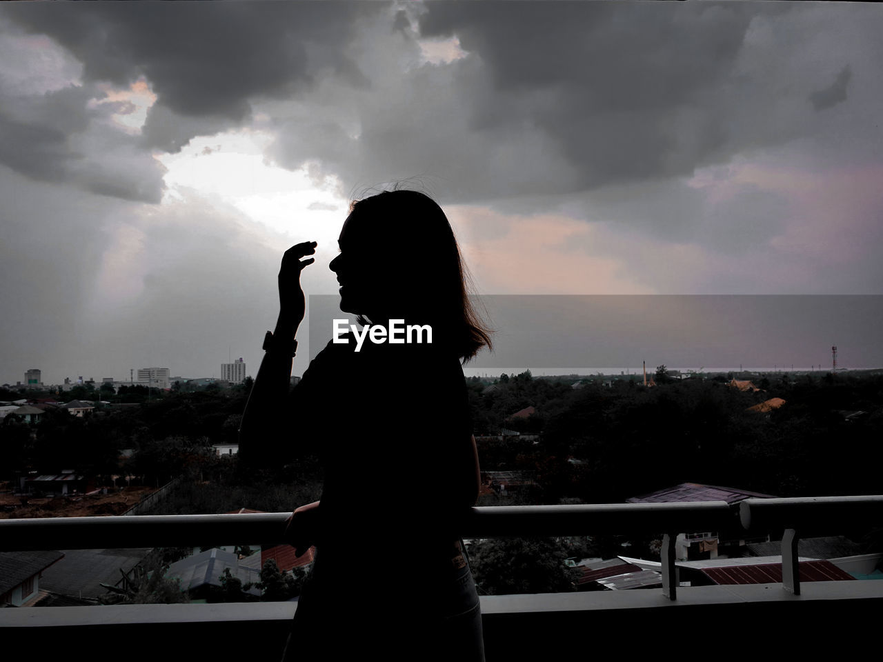 Side view of silhouette woman photographing cityscape against sky