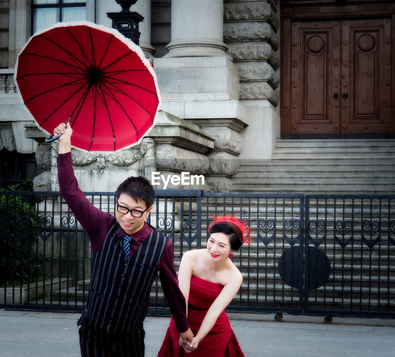 PORTRAIT OF A SMILING YOUNG WOMAN WITH RED UMBRELLA