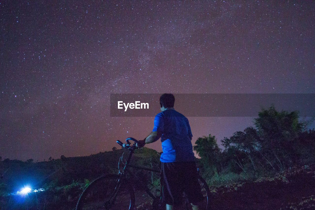 Rear view of man with bicycle against star field at night