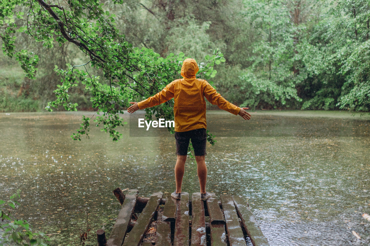 REAR VIEW OF BOY STANDING BY LAKE