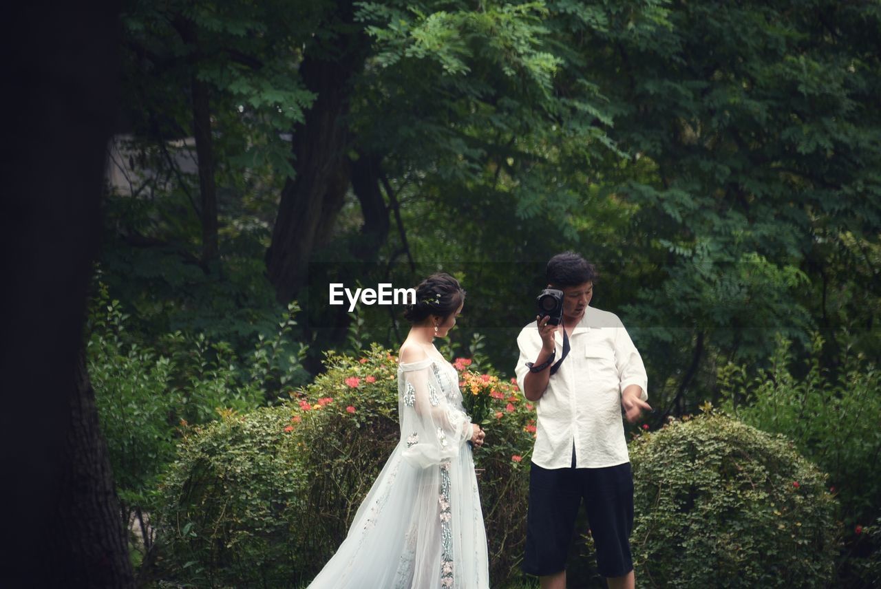 REAR VIEW OF WOMEN STANDING BY TREES