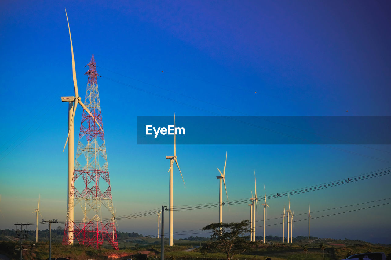 Low angle view of windmills against clear blue sky