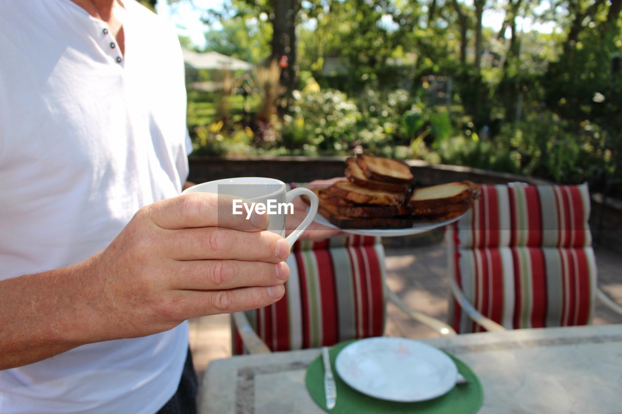 Midsection of man holding bread and coffee in balcony