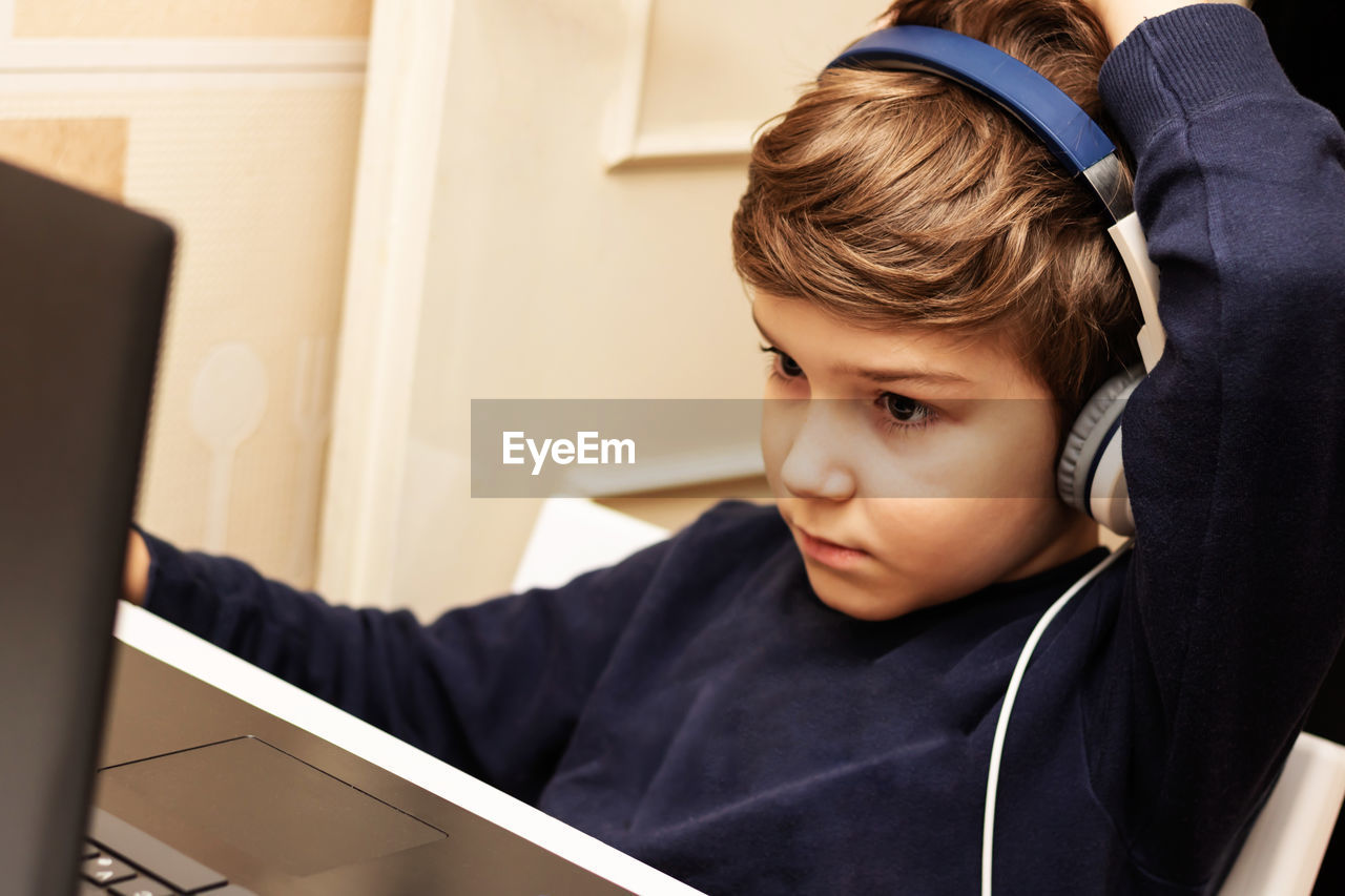 Small boy with headphones using computer during video call from home.