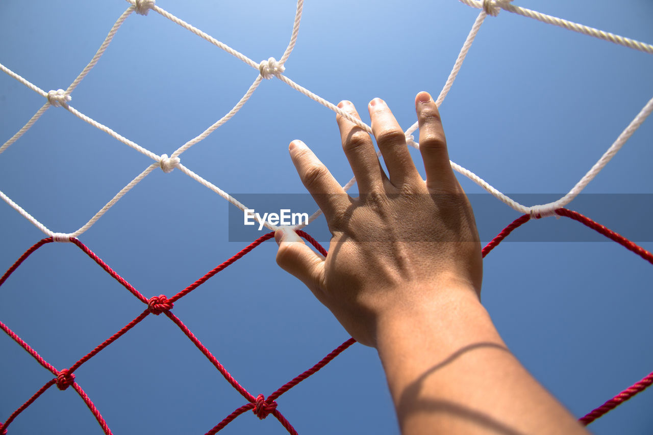 Cropped hand touching soccer net against clear sky