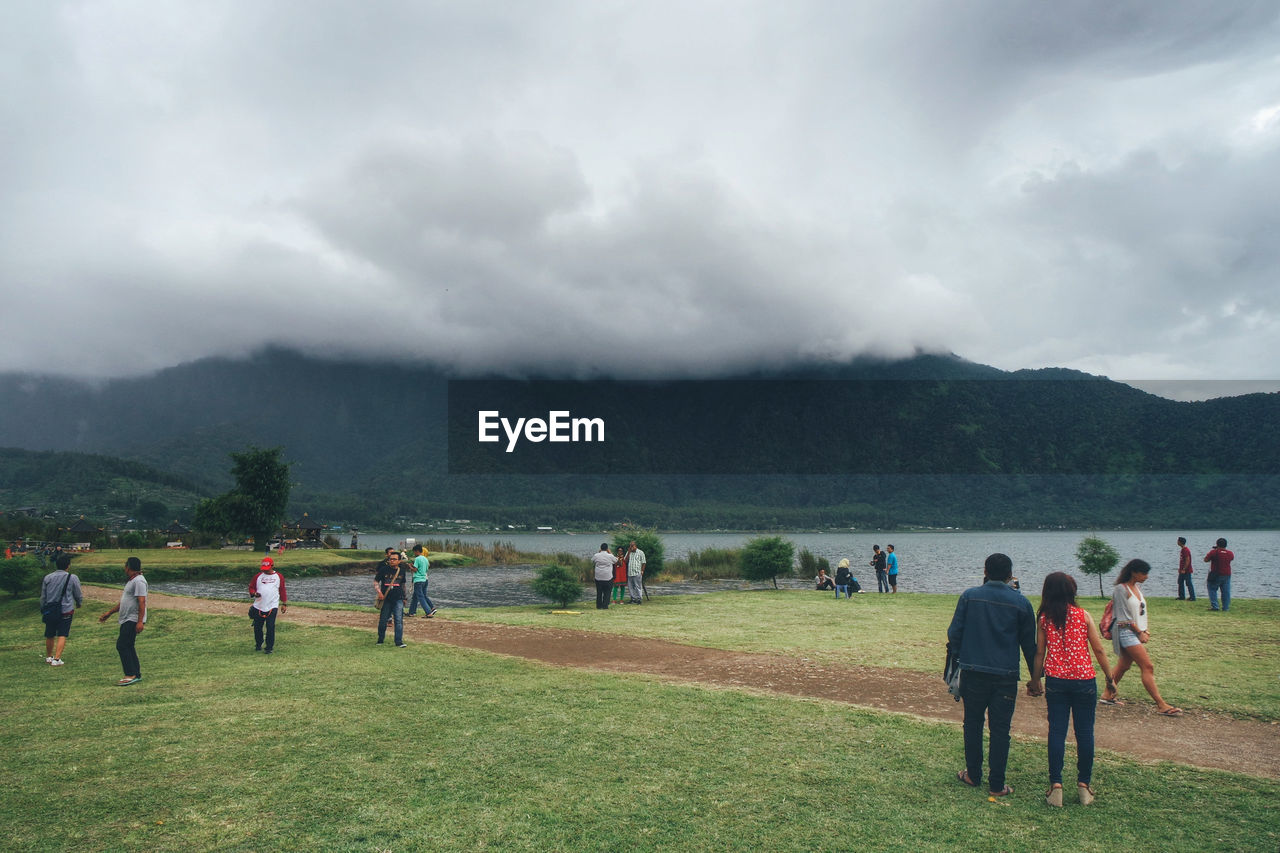 PEOPLE RELAXING ON COUNTRYSIDE LANDSCAPE AGAINST CLOUDY SKY