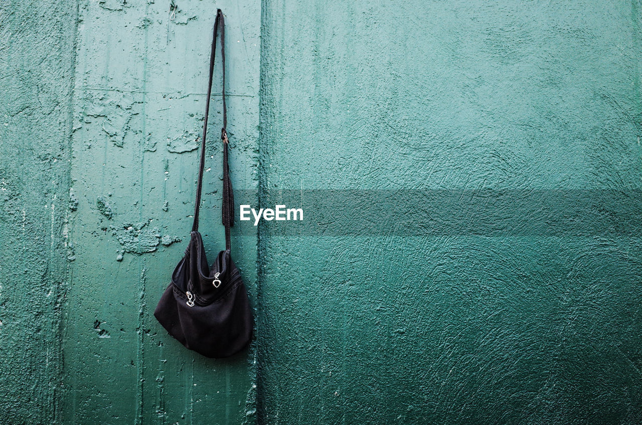 Black shoulder bag hanging from nail mounted on wall