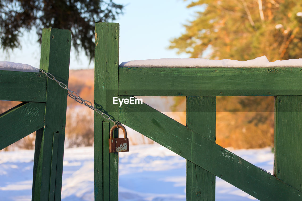 Close-up of padlock with chain on green wooden fence gate at winter sunny day lifght