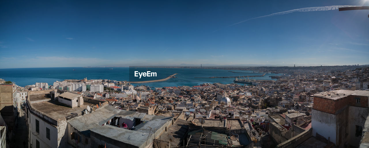 High angle view of townscape by sea against blue sky