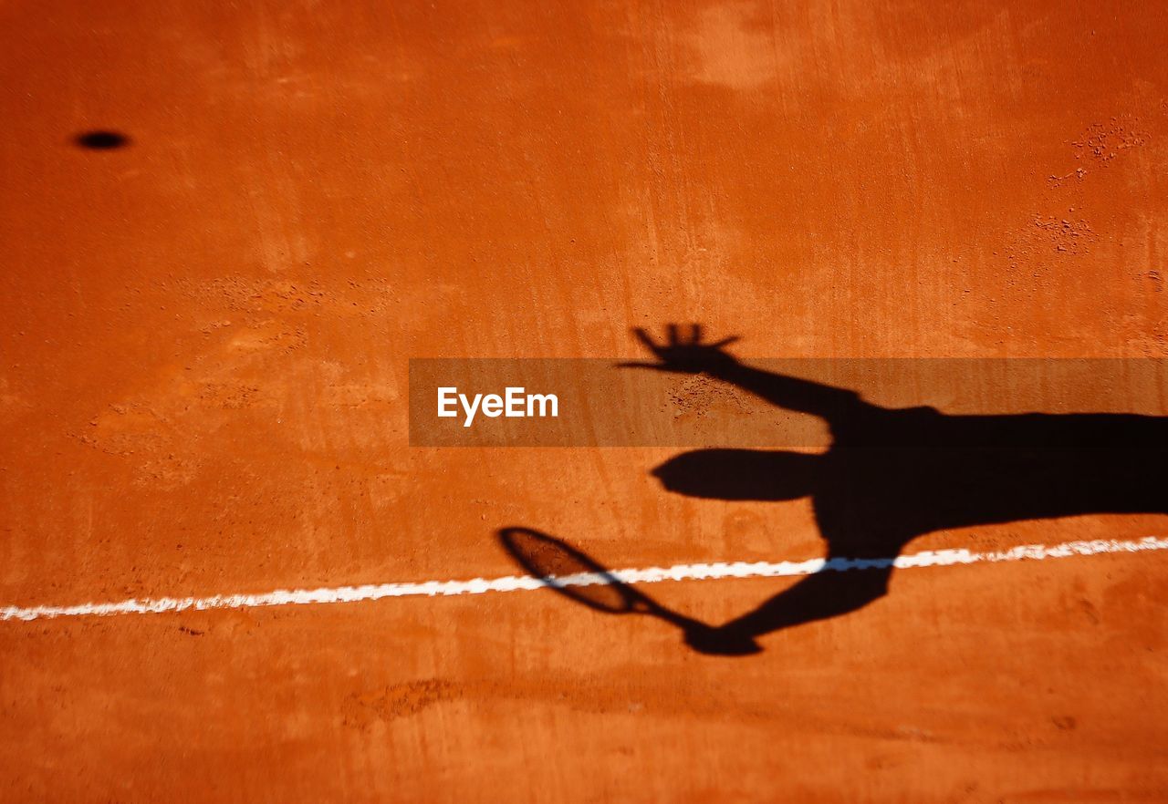 Shadow on man playing tennis on field
