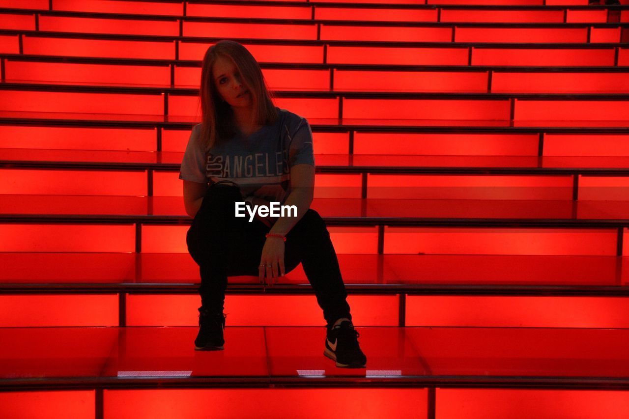 Portrait of young woman sitting on red illuminated steps