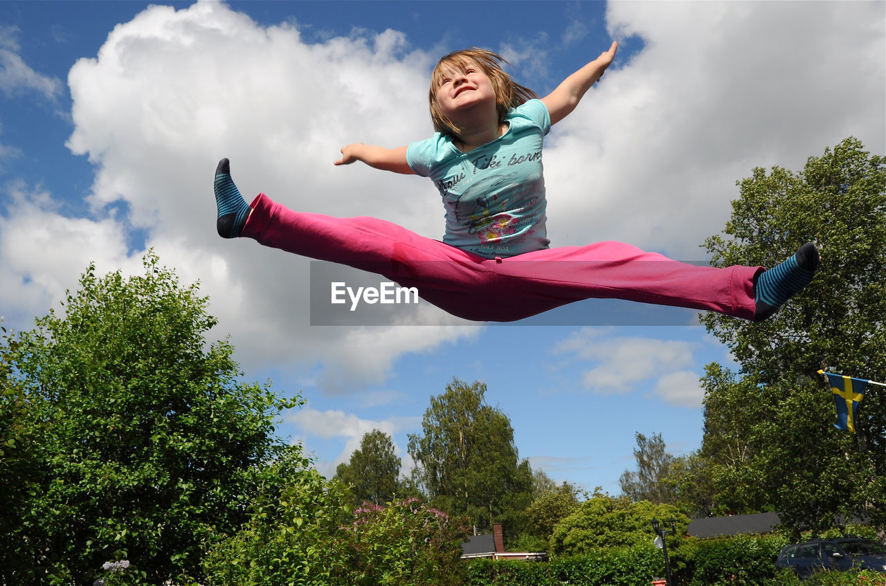 Low angle view of girl jumping over trees against sky