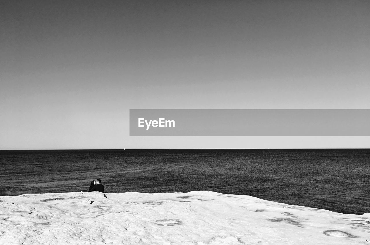 MAN STANDING ON SHORE AGAINST CLEAR SKY