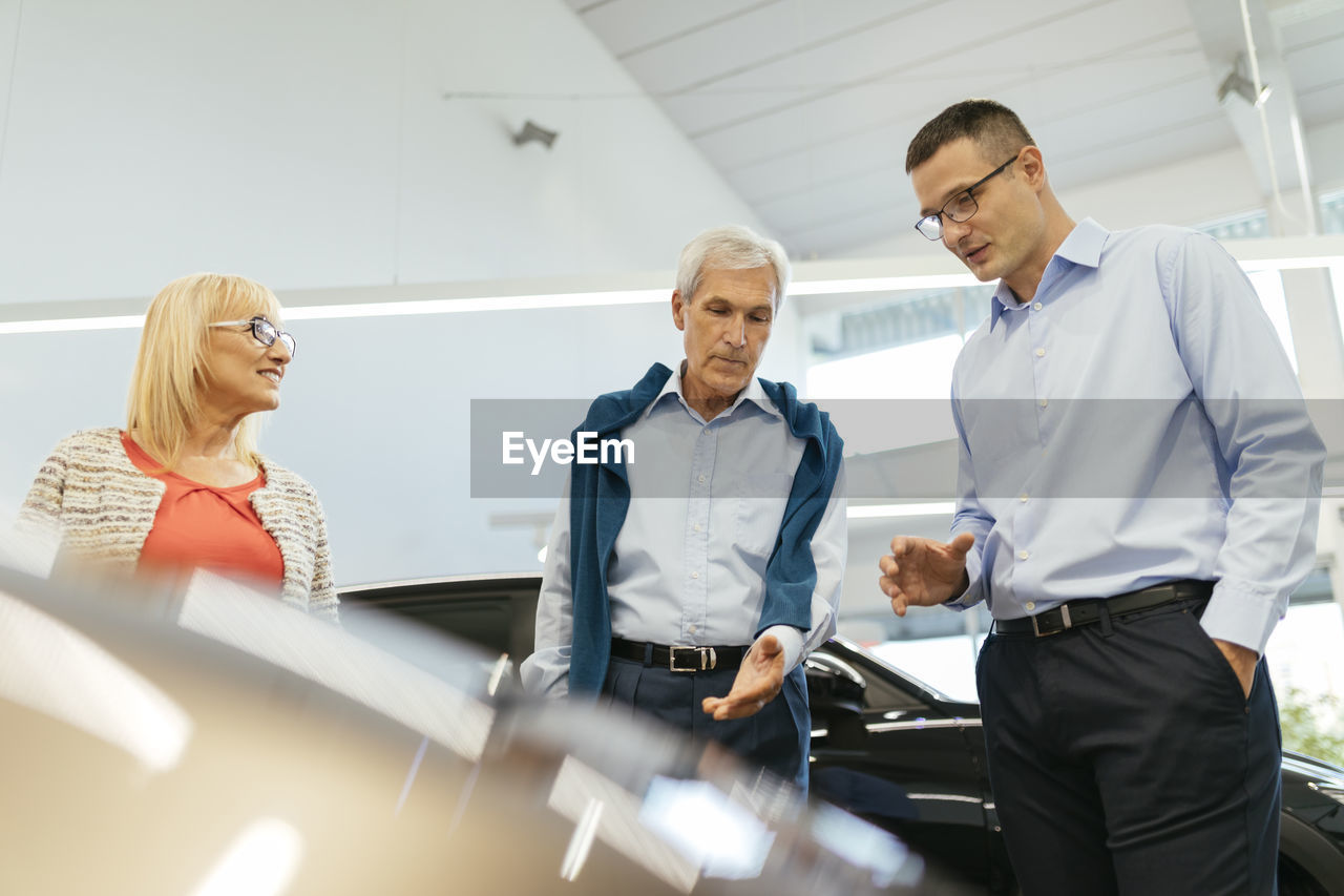 Senior couple couple talking with salesperson in car dealership