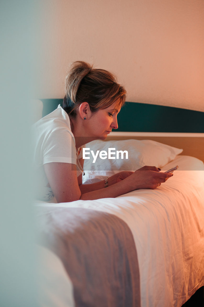 Woman using mobile phone on bed at home