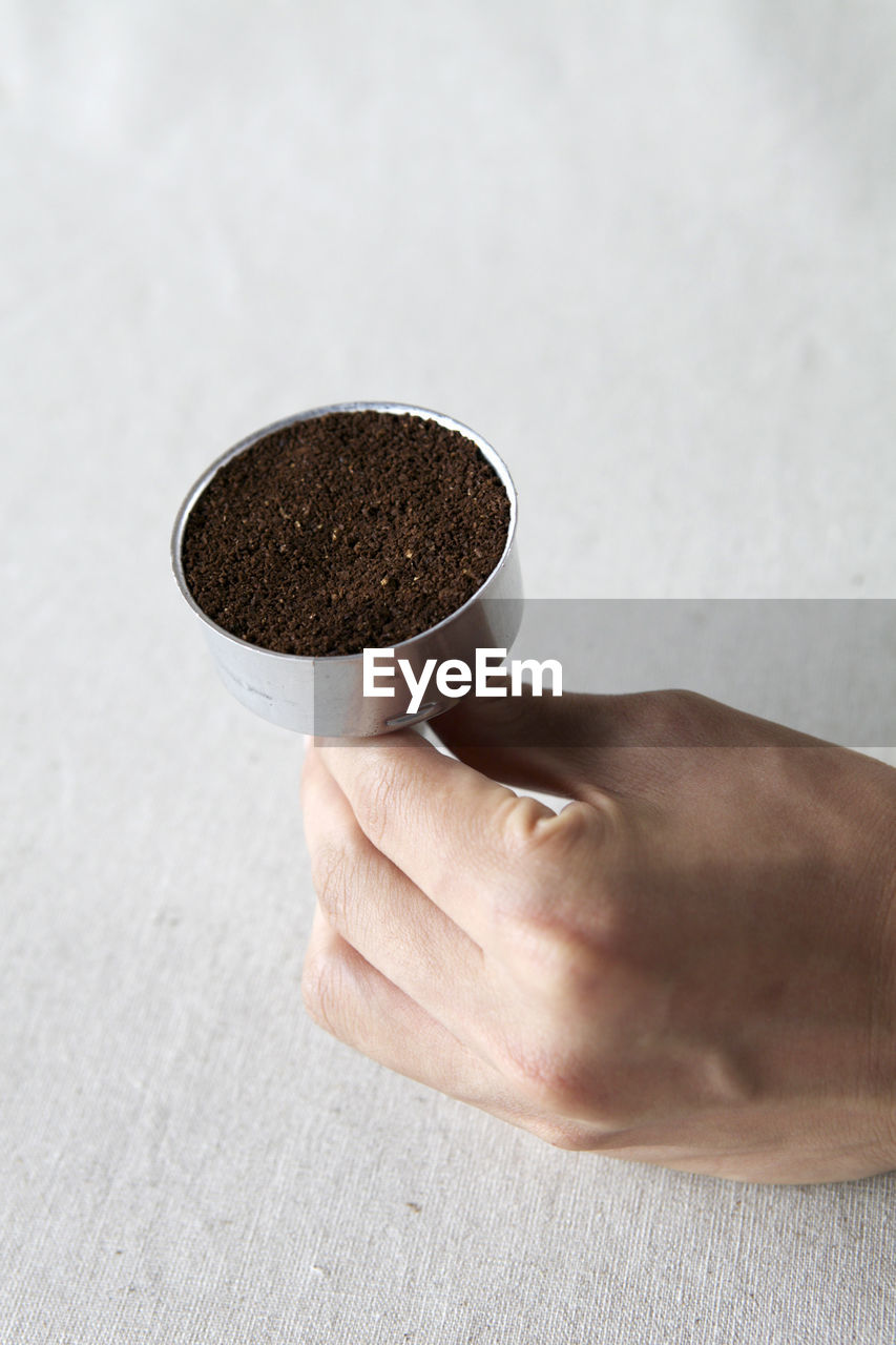 Cropped image of hand holding ground coffee in container at table