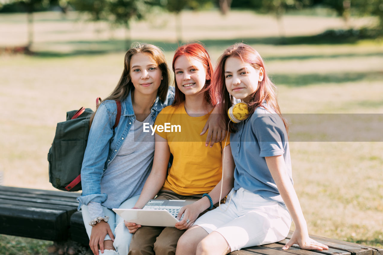A group of teenage girls is sitting on a park bench and preparing for classes together.