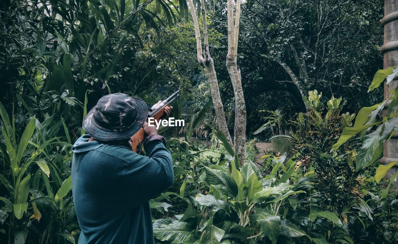 Rear view of man shooting with rifle against trees